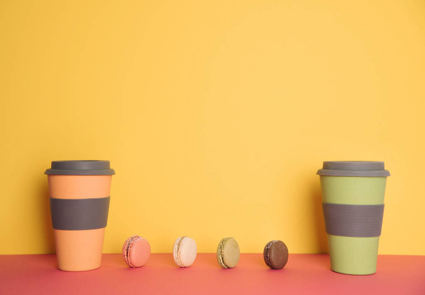 Cup of coffee to go with macaron on yellow and pink background - 写真・画像