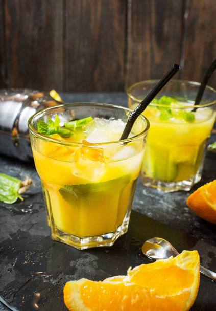 Холодний алкогольний літній цитрусовий коктейль з апельсином та м'ятою в окулярах та на фоні темного каменю. Коктейль робить барні інструменти, шейкер, листя м'яти
. - Фото, зображення