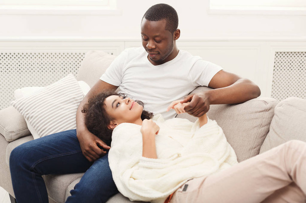 Smiling black couple having rest on sofa at home - Foto, immagini