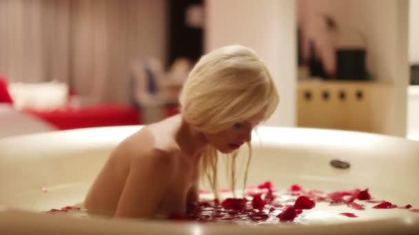eine sexy schöne Frau in einem großen Hotelbad voller Rosenblätter - Filmmaterial, Video