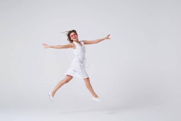 Chica juguetona haciendo gestos y sonriendo mientras salta contra el backgro
 - Foto, Imagen