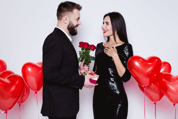 I congratulate you on the holiday of lovers. Smiling man giving flowers and gift to his happy woman on Valentine's Day. - Фото, зображення