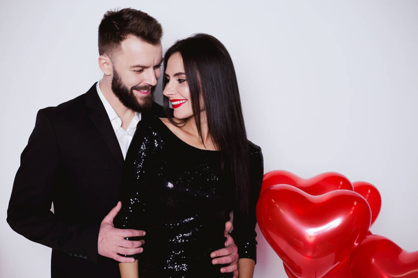 Beautiful young couple in love in black elegant costumes against a background of red balloons in the shape of a heart. Valentines day - Foto, imagen