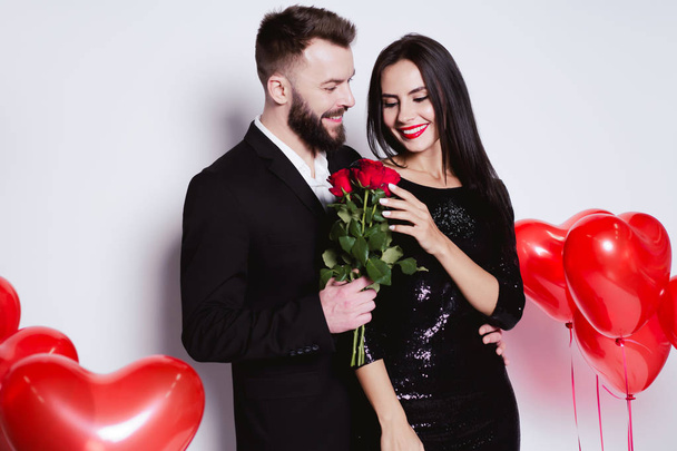 Beautiful happy smiling couple in love in chic costumes hugging and looking at the camera with flowers in hands. - Fotó, kép