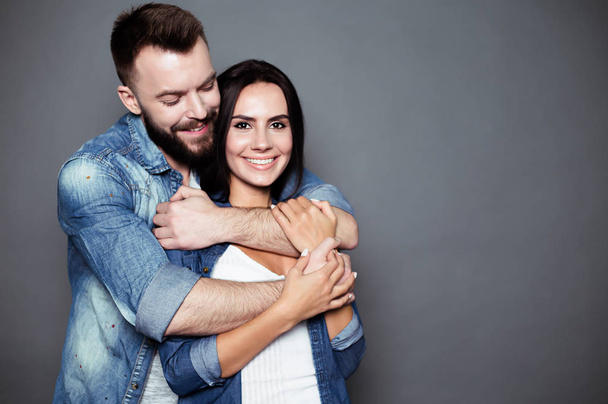 Beautiful and happy young couple in love or family in casual wear having fun and making fun of each other and posing on a gray background isolated. - Фото, зображення