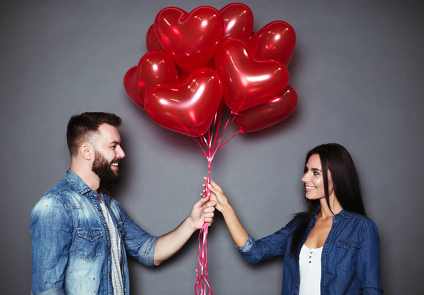 Beloved, this is for you. A handsome young man gives his smiling girl red heart-shaped balloons on St. Valentine's Day. - Fotó, kép