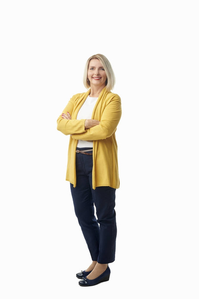Full length shot of a beautiful senior woman wearing casual clothes while standing with arms crossed at isolated white background. - Photo, image
