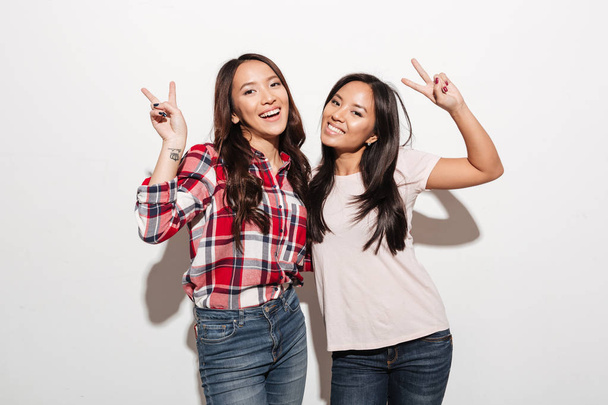 Two asian pretty cheerful ladies sisters showing peace gesture. - Фото, зображення