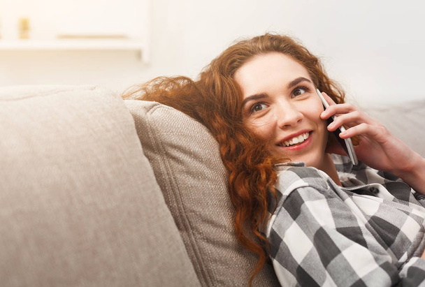 glücklich rothaarige Mädchen im Gespräch auf Handy auf dem Sofa - Foto, Bild