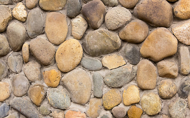 kő macskaköves lekerekített szürke bézs mintás háttérrel része egy régi épület a falon - Fotó, kép