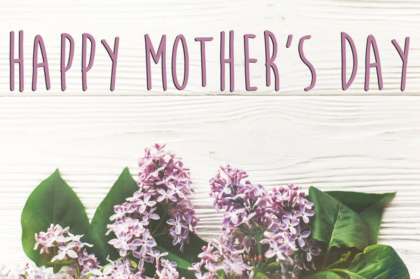 happy mother's day greeting card with tender lilac flowers branch on white wooden background  - Photo, Image