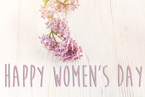 ευτυχισμένος γυναικών μέρα ευχετήρια κάρτα με πανέμορφο λιλά λουλούδια σε άσπρο φόντο ξύλινη, κάτοψη. - Φωτογραφία, εικόνα