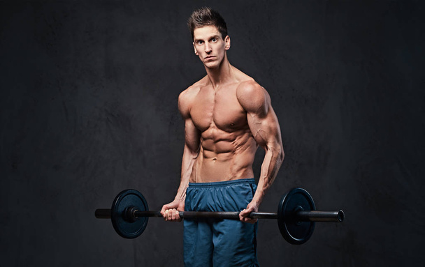 Entrenamiento de barra de bíceps masculino sin camiseta atlética sobre fondo gris
. - Foto, Imagen