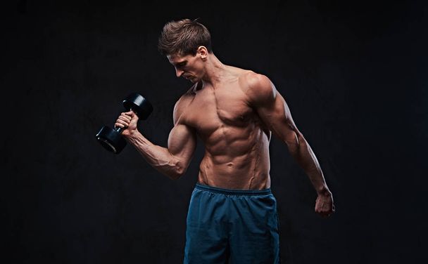 Exercice d'haltère biceps masculin sans chemise athlétique sur un backgroud gris foncé
. - Photo, image