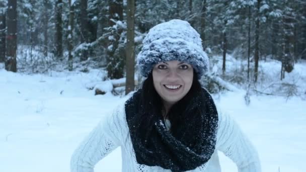 Grappig speels meisje gooien sneeuwbal rechtstreeks naar camera, witte spatten vliegen rond. Bedriegt rond in de sneeuw en de wandelingen in het bos. Sneeuw langzaam naar beneden vallen. - Video