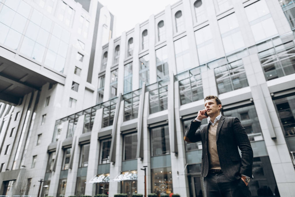 Образ харизматичного молодого бізнесмена, який розмовляє на смартфоні на відкритому повітрі біля бізнес-центру
 - Фото, зображення