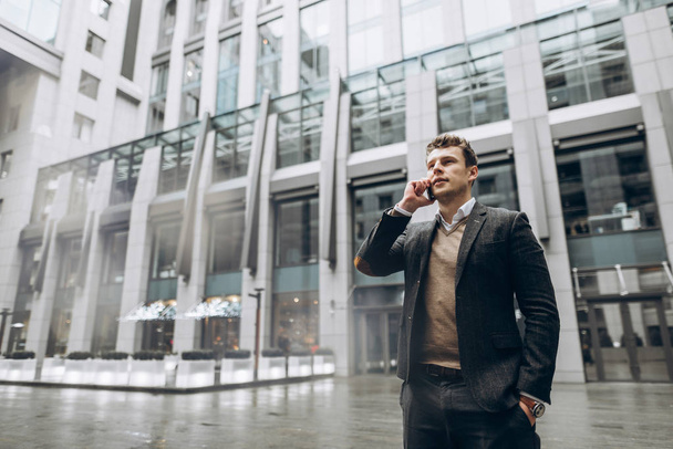 Portrait of a charismatic young businessman who talks on a smartphone outdoors near the business center - Valokuva, kuva
