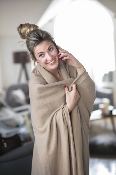 Mooie jonge vrouw op middelbare leeftijd op woonkamer is voorzien van deken lacht in de middag. Wintertijd. - Foto, afbeelding