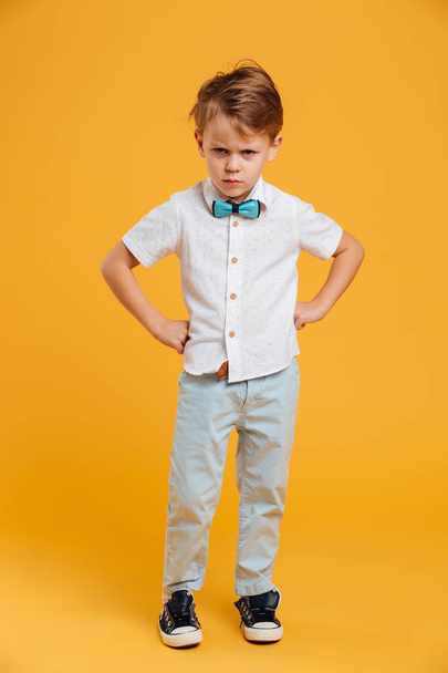 Angry little boy child standing isolated over yellow - 写真・画像