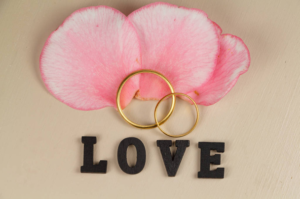 Dois anéis de casamento em ouro, pétalas rosa e amor
 - Foto, Imagem
