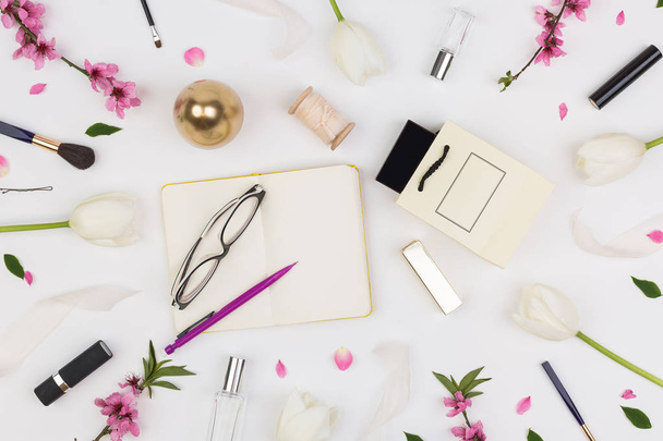 femininity, organisation, lifestyle concept. among white tulips and brunches of oriental cherry there are different cosmetics stuff and glasses with daily planner - Foto, imagen