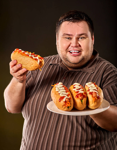 Gruby mężczyzna jedzenie fast food hot doga. Śniadanie dla osób otyłych. - Zdjęcie, obraz
