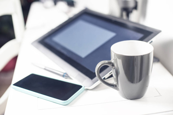 creative office white desk with graphic tablet, stylus, cell phone and a mug - Foto, Bild