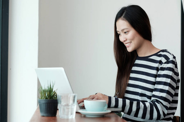 junge asiatische Frau benutzt Laptop-Computer, während sie beim Kaffee sitzt - Foto, Bild