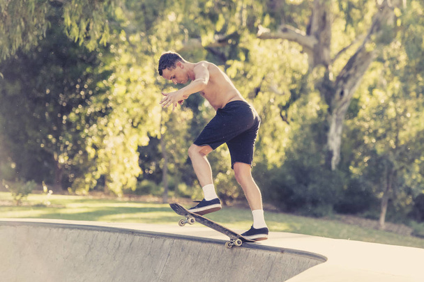 young American man in naked torso practicing radical skate board jumping and enjoying tricks and stunts in concrete half pipe skating track - Photo, Image