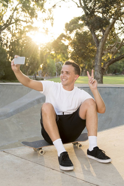 man 30s sitting on skate board after sport boarding training session taking selfie photograph portrait or picture on mobile phone  - Фото, изображение