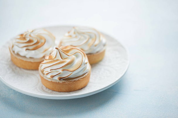 Delicious lemon tartlets with meringue on a white vintage plate. Sweet treat on a light blue background - Фото, зображення