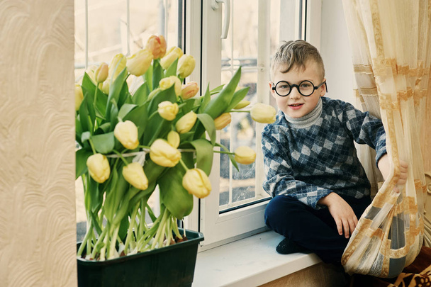 Ένα πραγματικά αξιολάτρευτο αγόρι σπίτι με τουλίπες. Τα παιδιά με τα λουλούδια που καλλιεργούνται στο σπίτι - Φωτογραφία, εικόνα