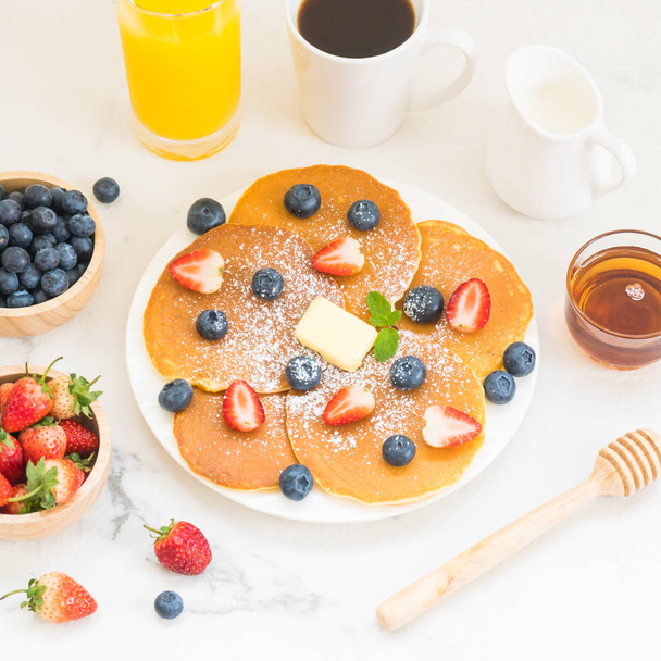 健康的な朝食は白い石のテーブル背景にパンケーキのブルーベリーとイチゴの果実とブラック コーヒー、牛乳、オレンジ ジュースとセット - 写真・画像