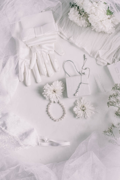 Białe akcesoria ślubne na tle ślubnym z perłami, białe satynowe wstążki i koronki, rękawiczki, bransoletka, płaski układ na blogu mody, widok z góry - Zdjęcie, obraz