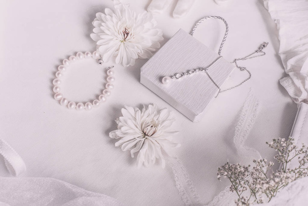 Λευκά νυφικά αξεσουάρ για φόντο γάμου με πέρλες, λευκές σατέν κορδέλες και δαντέλα, γάντια, βραχιόλι, επίπεδο lay για fashion blog, top view - Φωτογραφία, εικόνα