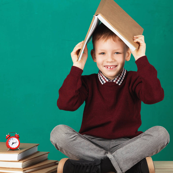 Iloinen hymyilevä pieni koulupoika, jolla on suuria raskaita kirjoja hänen h
 - Valokuva, kuva