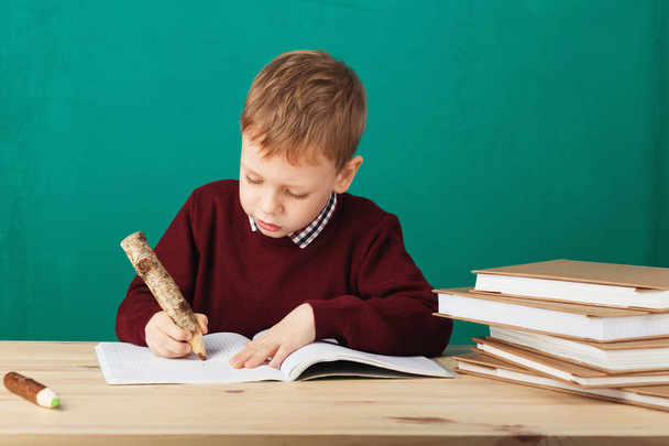 Улыбающийся маленький школьник пишет заметки в классе против зеленой ва
 - Фото, изображение
