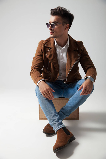 joven hombre de la moda sentado en una caja y mira hacia otro lado
 - Foto, imagen