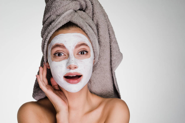 happy woman with a towel on her head applied a white cleansing mask on her face - Fotó, kép