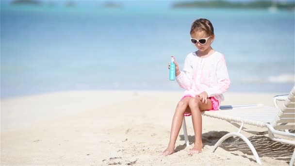 Schattig meisje met fles zonnebrandcrème zit op tropisch strand - Video