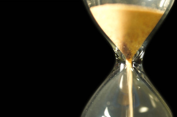 Sand running through the bulbs of an hourglass measuring the passing time in a countdown to a deadline, on a black background with copy space for your text. - Photo, Image