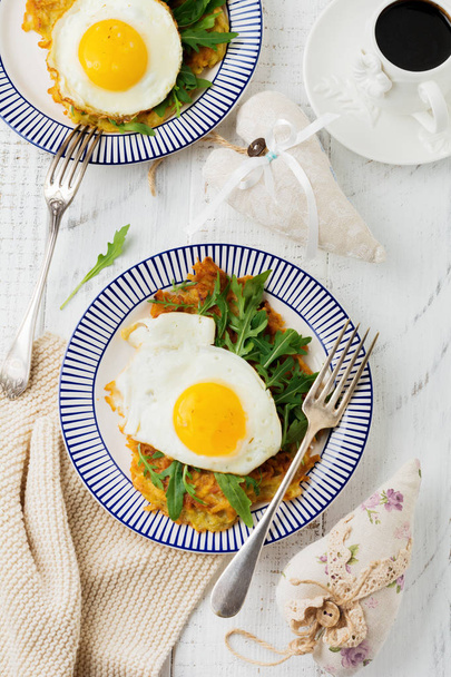 Fried egg with potato pancake, arugula and avocado on ceramic plate for breakfast on white wooden table background. Selective focus. Top view. Copy space. - Photo, image
