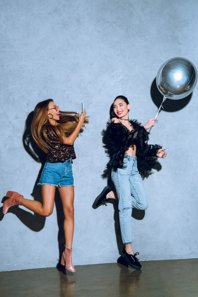 stylish african american girl with smartphone photographing asian friend having fun with balloon at party - Foto, Bild