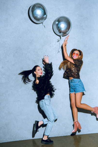 красивые стильные мультиэтнические женщины веселятся с серебряными воздушными шарами и улыбаются в камеру
 - Фото, изображение