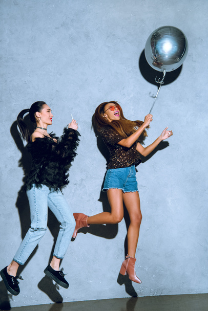 hermosas chicas multiétnicas con estilo que se divierten con globo y teléfono inteligente en la fiesta
  - Foto, imagen
