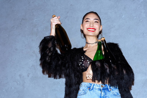 mode heureux asiatique fille tenant bouteilles avec boissons alcoolisées sur gris
 - Photo, image
