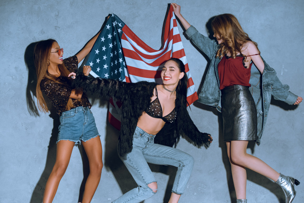 multicultural young women with american flag against concrete wall - Foto, Imagen