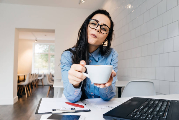 a woman in glasses sits at a table and drinks coffee - Foto, immagini