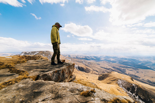 Mies turisti seisoo taustalla vuorten aurinkoisena päivänä
 - Valokuva, kuva