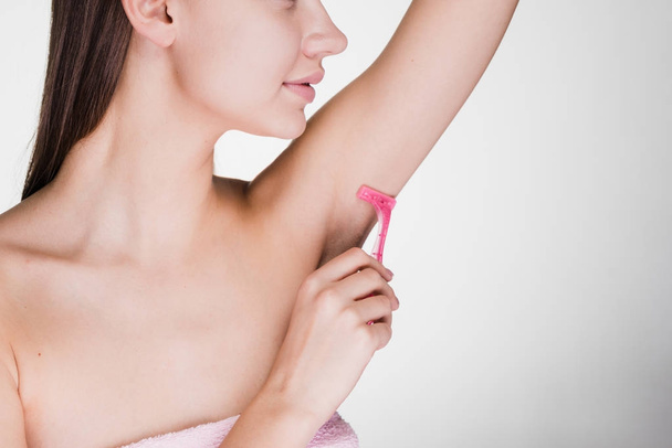 the woman on a gray background conducts a depilation of armpits with the razor - Foto, afbeelding